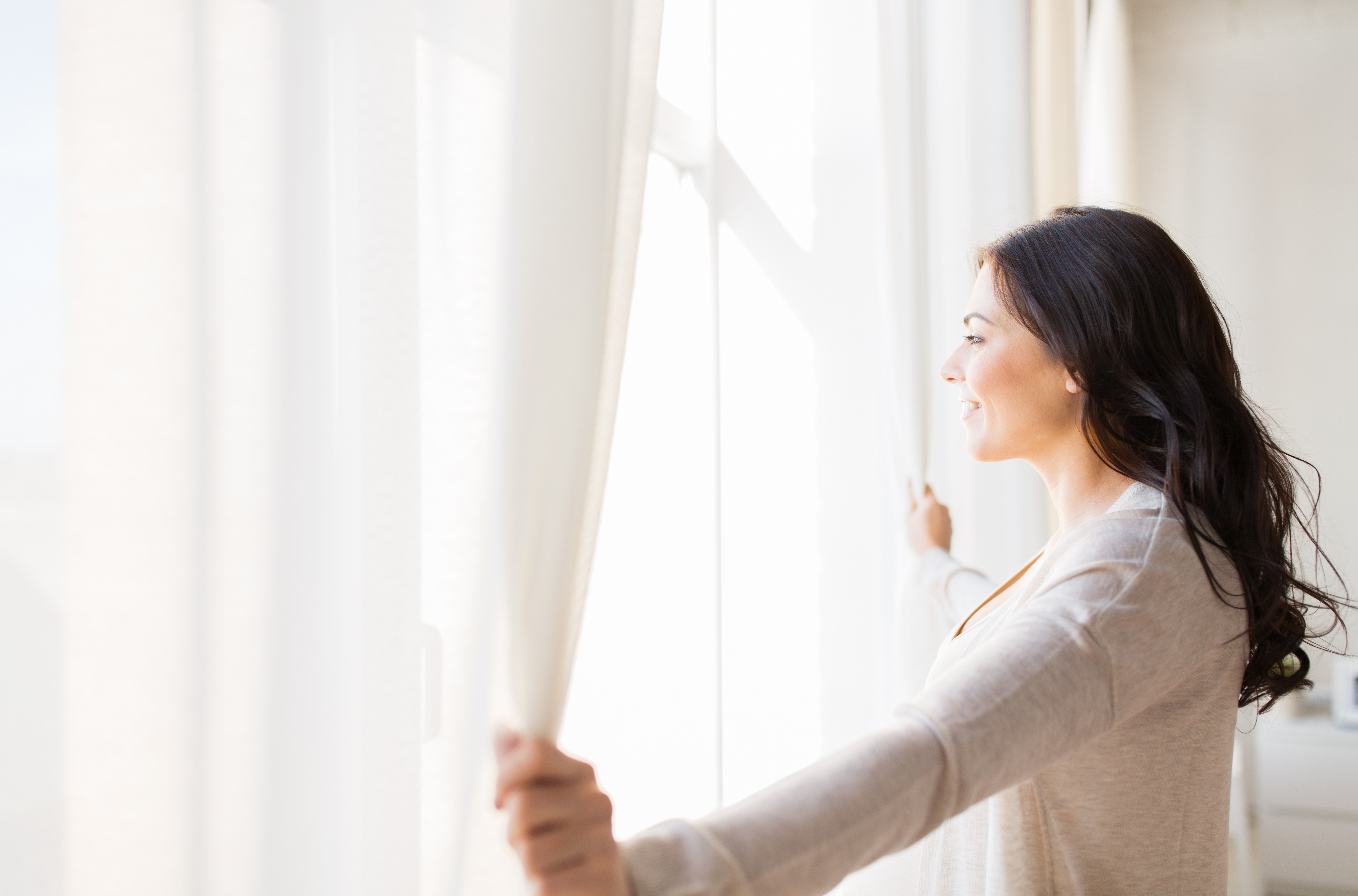 woman opening curtains to window looking into sun